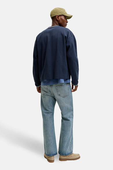 Blauwe sweater van ORIGINALS BY JACK & JONES, met een gestreepte geribde kraag en manchetten, gedragen met een spijkerbroek en beige schoenen.