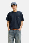 T-shirt à manches courtes bleu PREMIUM BLUE van JACK & JONES, gedragen met een camelkleurige jas, een wijde jeans en bootschoenen.
