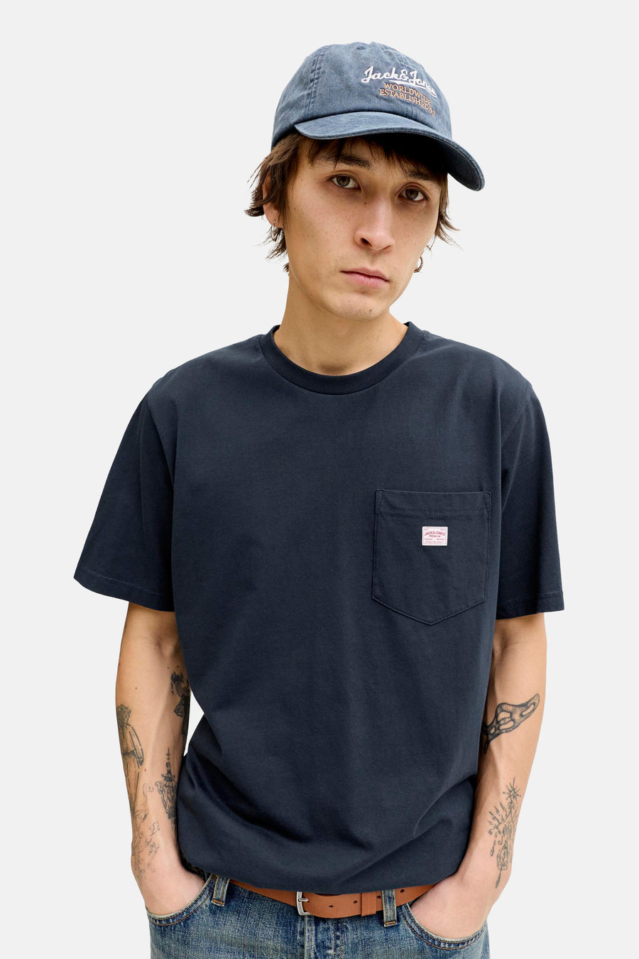 Blauw T-shirt met korte mouwen van PREMIUM BLUE by JACK & JONES, met borstzak, gedragen met een spijkerbroek en een pet.