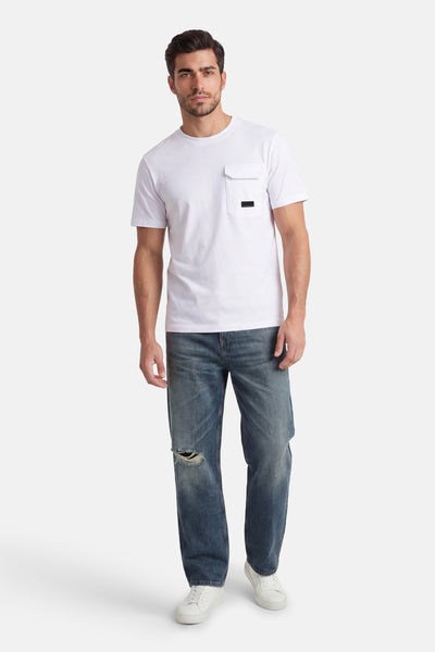 T-shirt à manches courtes blanc de JACK & JONES, avec une poche poitrine et porté avec un jean délavé déchiré.