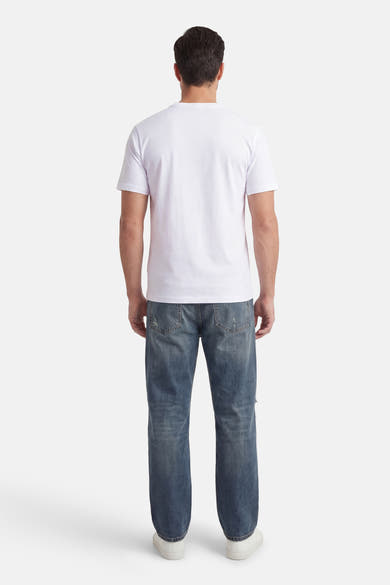 T-shirt à manches courtes blanc de Jack & Jones, porté avec un jean bleu délavé et des chaussures blanches.