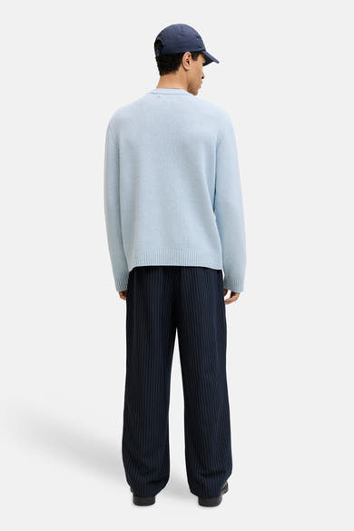 Ronde hals trui blauw van ORIGINALS BY JACK & JONES, gedragen met een broek met verticale strepen en een pet.