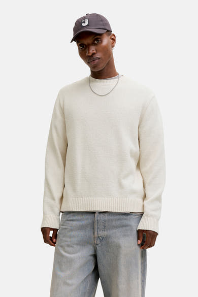 Ecru ronde hals trui van ORIGINALS BY JACK & JONES gedragen met een zwart leren jasje en een wijde jeans.