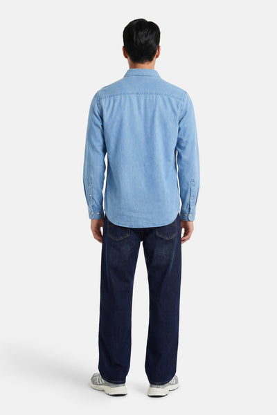 Blauwe spijkerblouse van PREMIUM by JACK & JONES, van achteren gezien op een mannelijk model met een donkere spijkerbroek en sneakers.