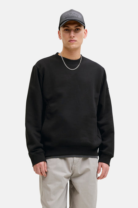 Zwarte sweater van JACK & JONES, gedragen met een beige broek en een zilveren ketting.