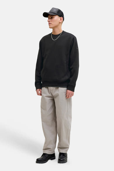Zwarte rondehals sweatshirt van JACK & JONES, gedragen met een beige broek en zwarte schoenen.