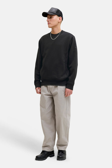 Zwarte rondehals sweatshirt van JACK & JONES, gedragen met een beige broek en zwarte schoenen.
