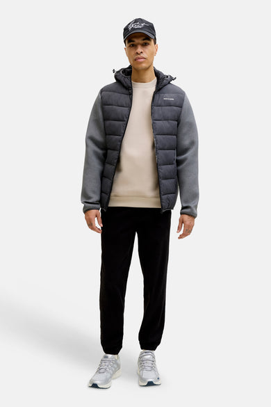 Sweat-shirt beige à col rond de Jack & Jones, porté avec une veste matelassée noire et un pantalon de survêtement noir.