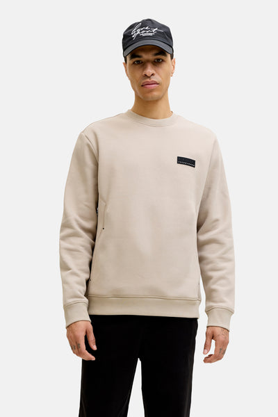 Beige rondehals sweatshirt van JACK & JONES, met een zwart embleem op de borst.