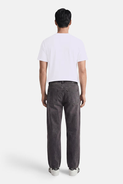 White short-sleeve t-shirt from back view, plain cotton with rounded neckline, worn with dark gray jeans and white sneakers