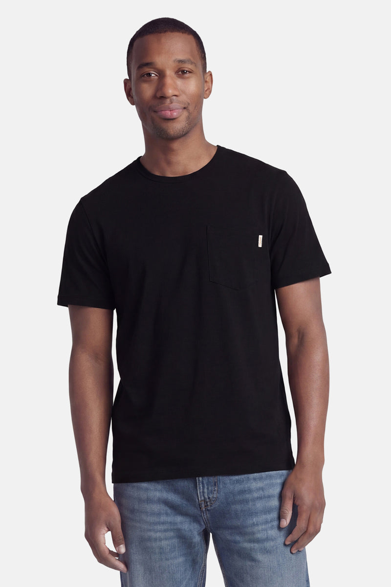 Black short-sleeve t-shirt with chest pocket and small white label, worn by model in front view with blue jeans.