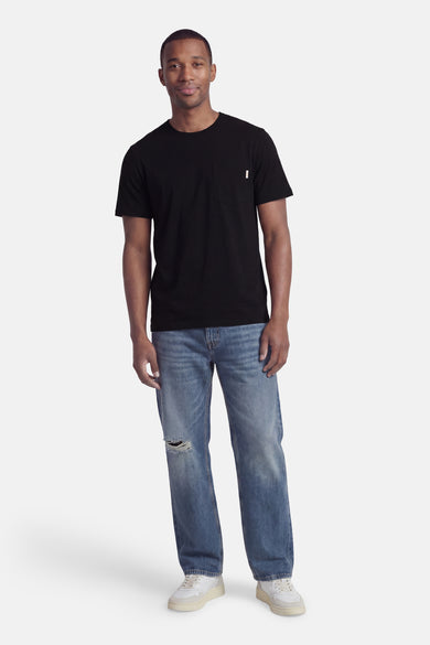 Black short-sleeve t-shirt with chest pocket, worn by model in full-length lifestyle view with distressed jeans and white sneakers.