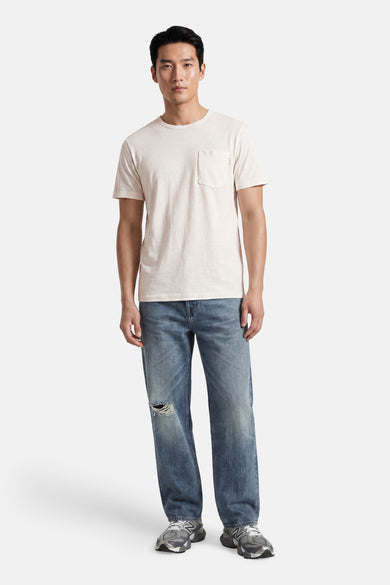 Off-white short-sleeve t-shirt with chest pocket, worn by model in full-length lifestyle view with distressed jeans and sneakers.