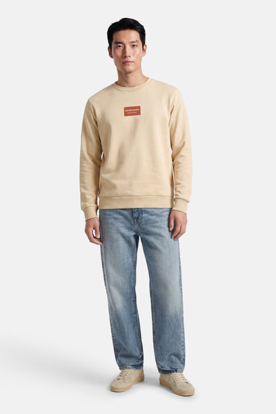 Sweat-shirt col rond beige de JACK & JONES, porté avec un jean bleu et des baskets beiges.