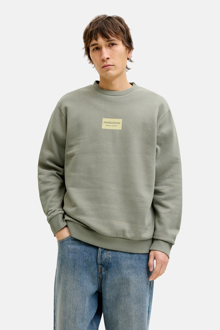 Sweat-shirt vert col rond de Jack & Jones, avec un logo carré sur la poitrine, porté avec un jean bleu.