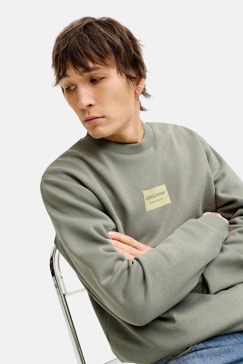 Groene sweater met ronde hals van Jack & Jones, met een logopatch op de borst, gedragen met een blauwe jeans.