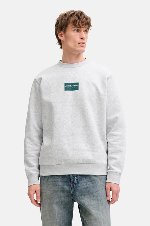 Gemêleerd grijs sweatshirt van JACK & JONES, met groen logo-patch, gedragen met een blauwe spijkerbroek en beige bootschoenen.