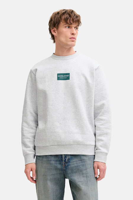Sweat col rond gris de Jack & Jones, avec un logo carré sur le devant, porté avec un jean.
