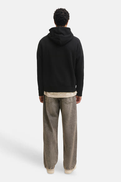 Black hooded sweatshirt back view, soft fleece texture, ribbed cuffs and hem, worn with light beige shirt and gray wide-leg jeans
