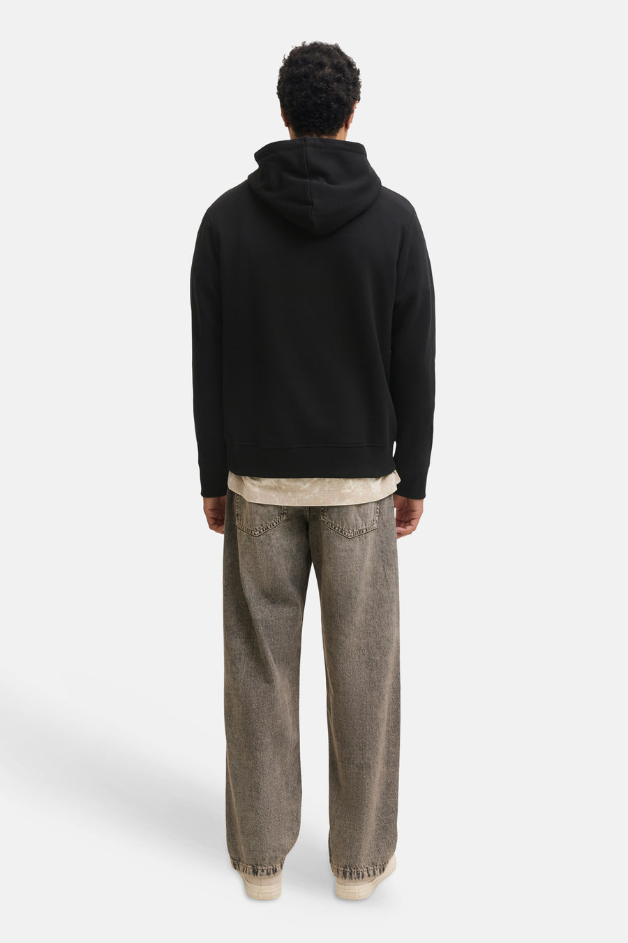 Black hooded sweatshirt back view, soft fleece texture, ribbed cuffs and hem, worn with light beige shirt and gray wide-leg jeans