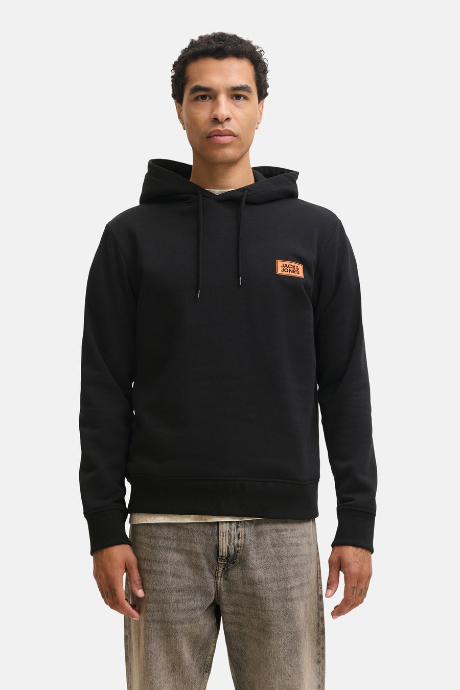 Black hooded sweatshirt by Jack & Jones with orange logo patch on chest, front view, worn with acid-wash jeans