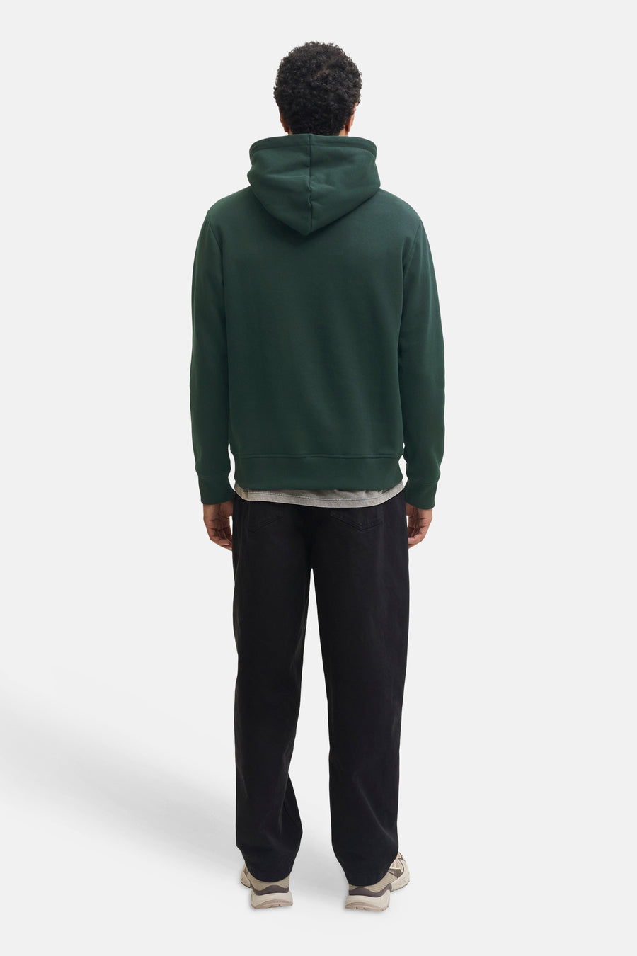 Dark green hooded sweatshirt by Scarab, back view, ribbed cuffs and hem, worn with black pants and beige sneakers.