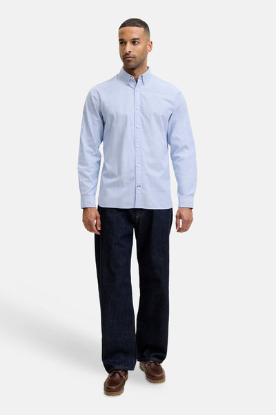 Light blue long-sleeve button-down shirt with classic collar, worn by model in full-length front view with dark jeans and brown shoes.