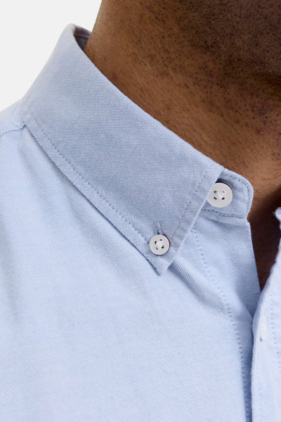 Light blue long-sleeve shirt with textured fabric and white buttons, close-up view of collar and neck area