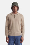 Beige ribbed knit polo sweater with button placket and collar, worn with olive cap and blue jeans, front view