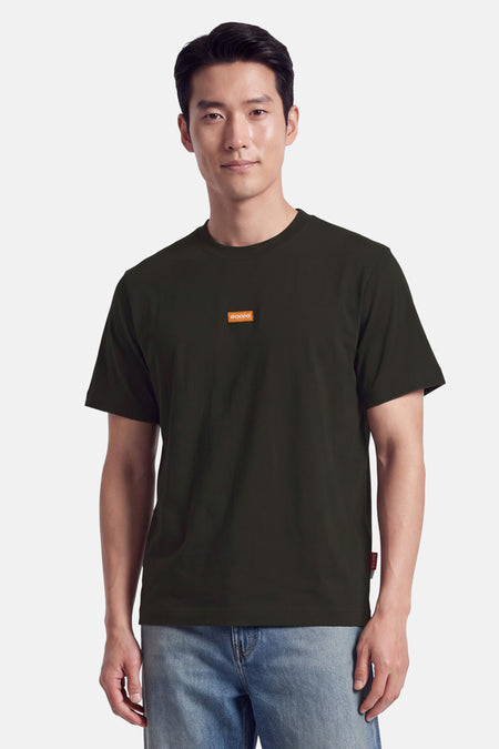 T-shirt vert à manches courtes de JACK & JONES, col rond, patch orange sur poitrine, porté avec jeans bleus, vue frontale.