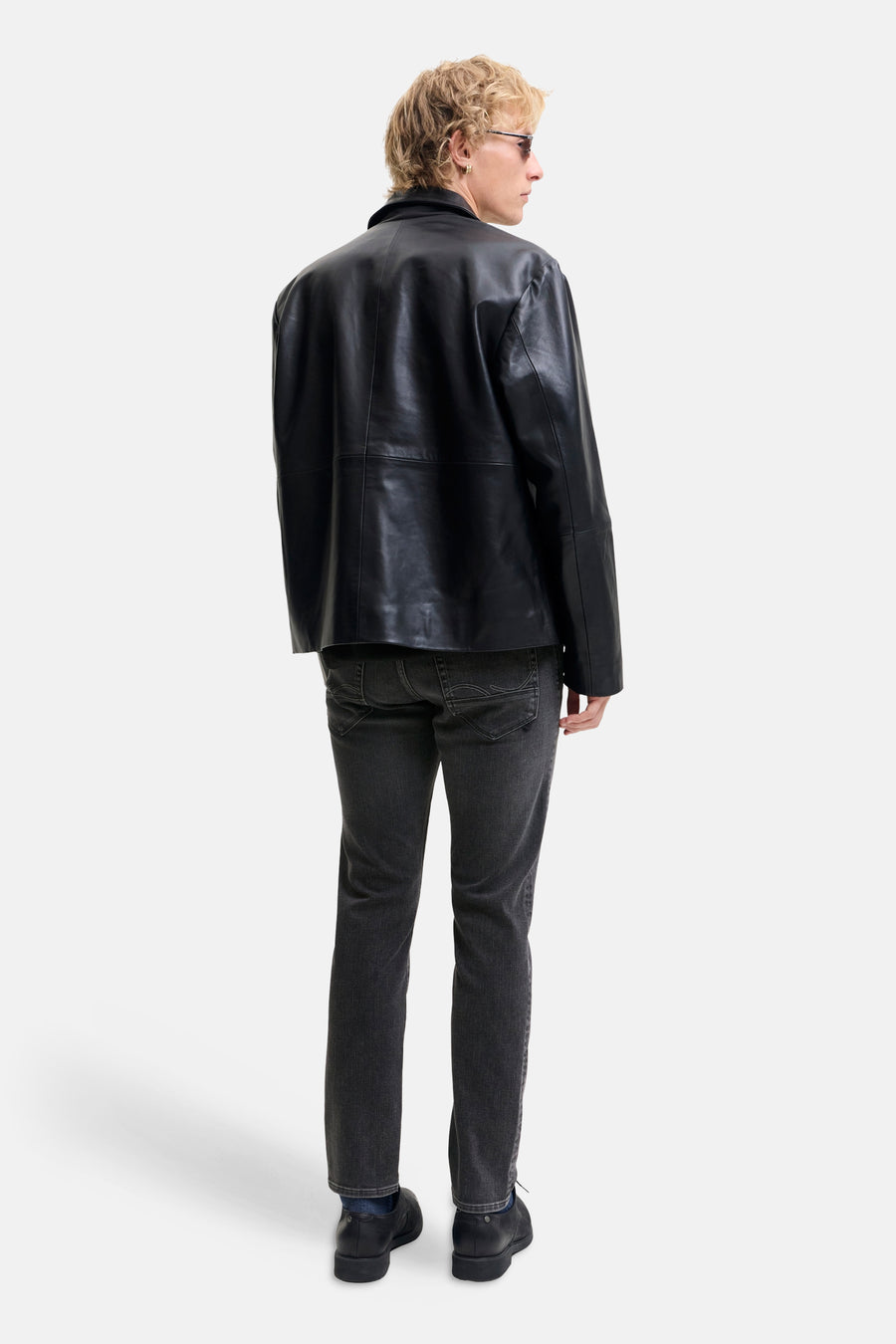 Black slim-fit denim jeans by Glenn, shown from back view with subtle fading and stitched back pockets, paired with black leather jacket and shoes.