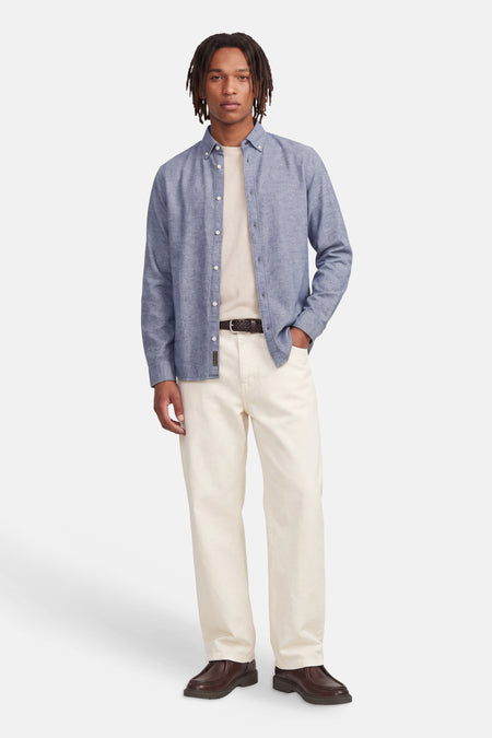 Blue long-sleeve button-down shirt with textured fabric, worn open over cream tee, paired with off-white trousers and brown leather shoes, full-body front view