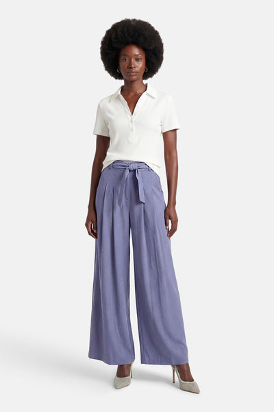 Blauwe Terra di Siena pantalon met wijde pijpen en strikceintuur, gedragen met een witte polo en pumps met pailletten.