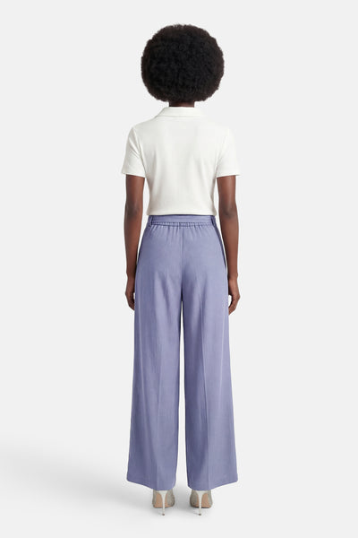 Pantalon de tailleur bleu Terra di Siena, coupe ample, porté avec un polo blanc et des escarpins à paillettes, vue de dos.