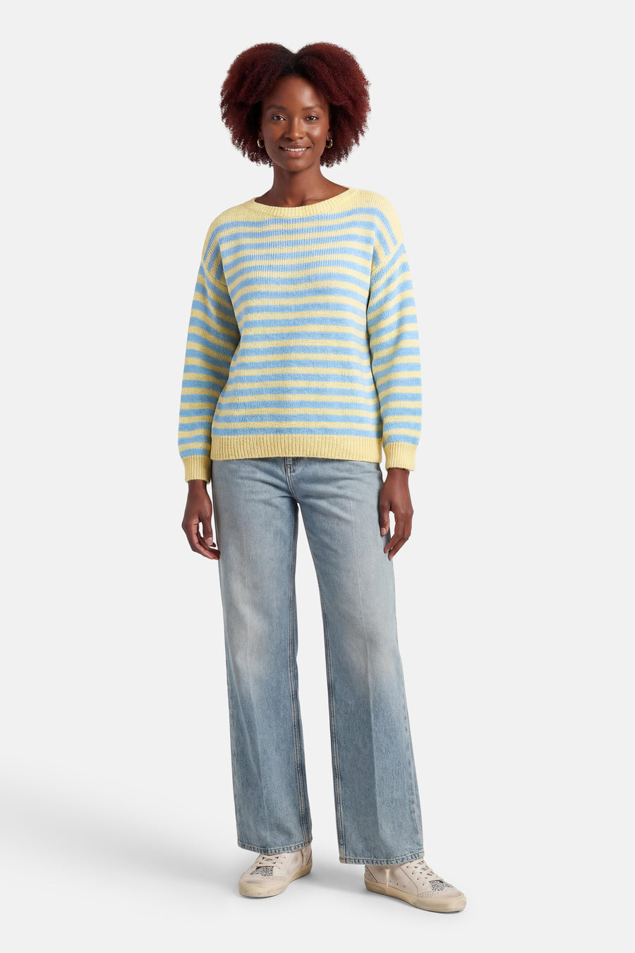 Multigekleurde Terra di Siena trui met blauwe en gele horizontale strepen, gedragen met een wijde blauwe jeans en crèmekleurige sneakers.