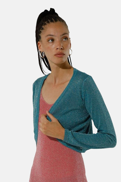 Gilet turquoise de GOA GOA, à manches longues, porté sur une robe moulante rose scintillante.