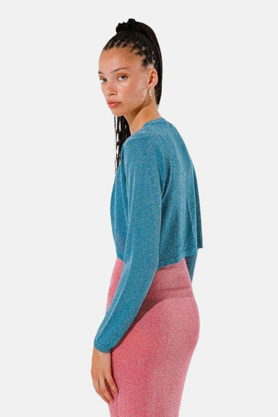 Gilet turquoise de GOA GOA, porté avec une jupe rose pailletée, vu de côté.
