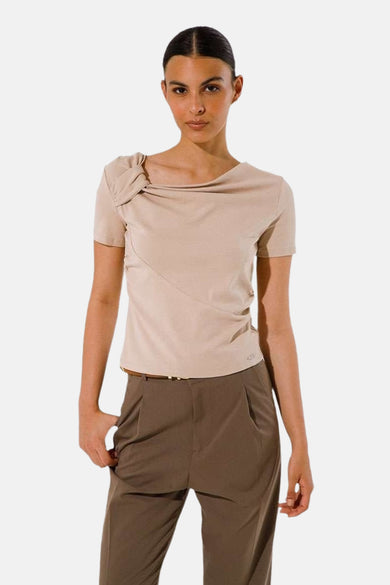 T-shirt à manches courtes beige de GOA GOA, avec un détail noué sur l'épaule et porté avec un pantalon marron.
