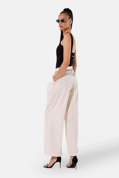Pantalon de costume beige de GOA GOA, ample et taille haute, porté avec un débardeur noir et des escarpins.