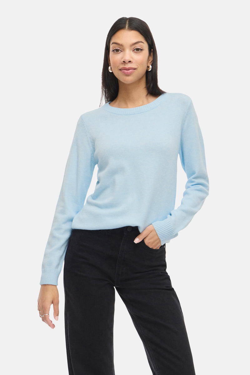 Pull à col rond bleu van VILA®, porté avec un pantalon noir et des boucles d'oreilles argentées.