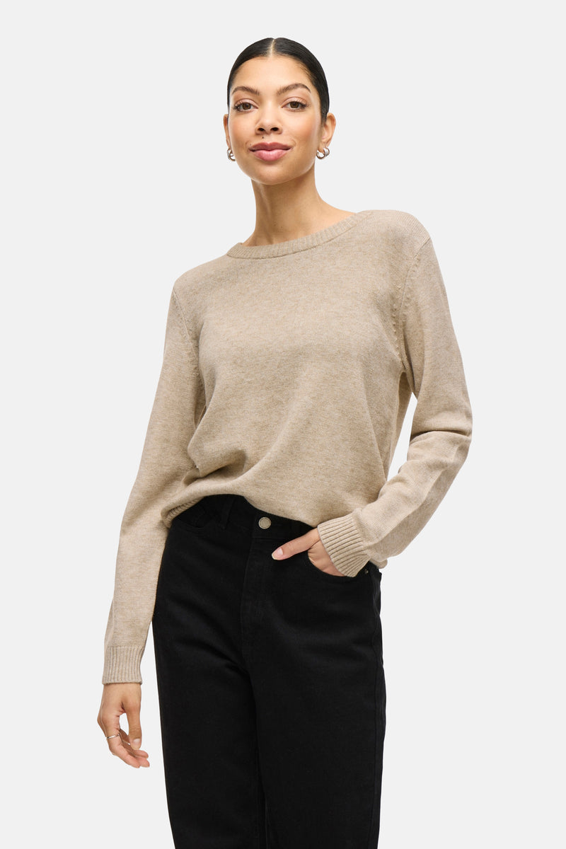 Pull beige de VILA, porté avec un pantalon noir, la main dans la poche.