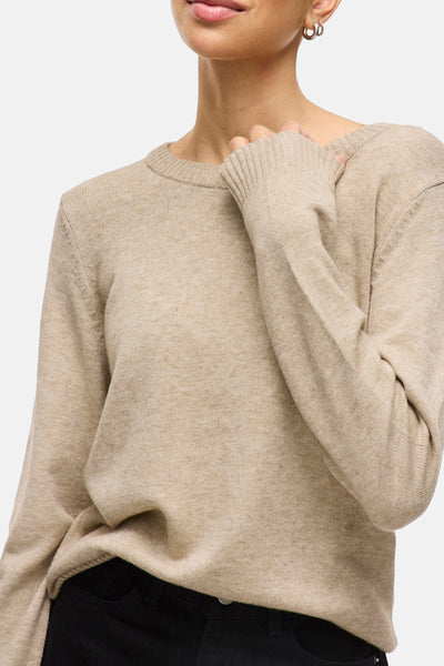 Pull beige de VILA, avec des manches longues et porté avec un pantalon noir.