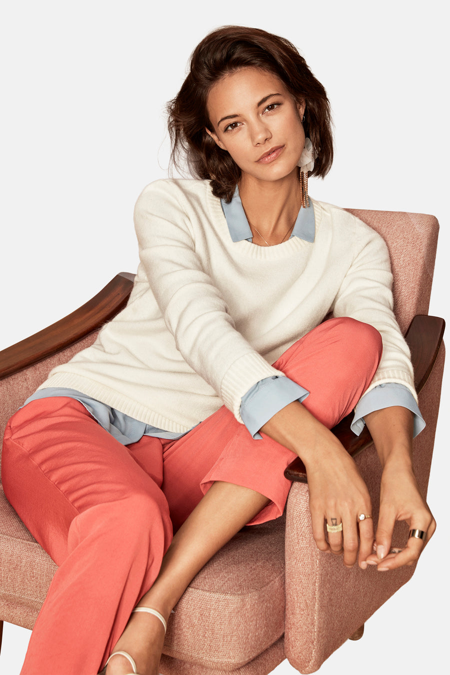Pull col O blanc de VILA, porté avec une chemise bleu clair et un pantalon corail, assis dans un fauteuil.