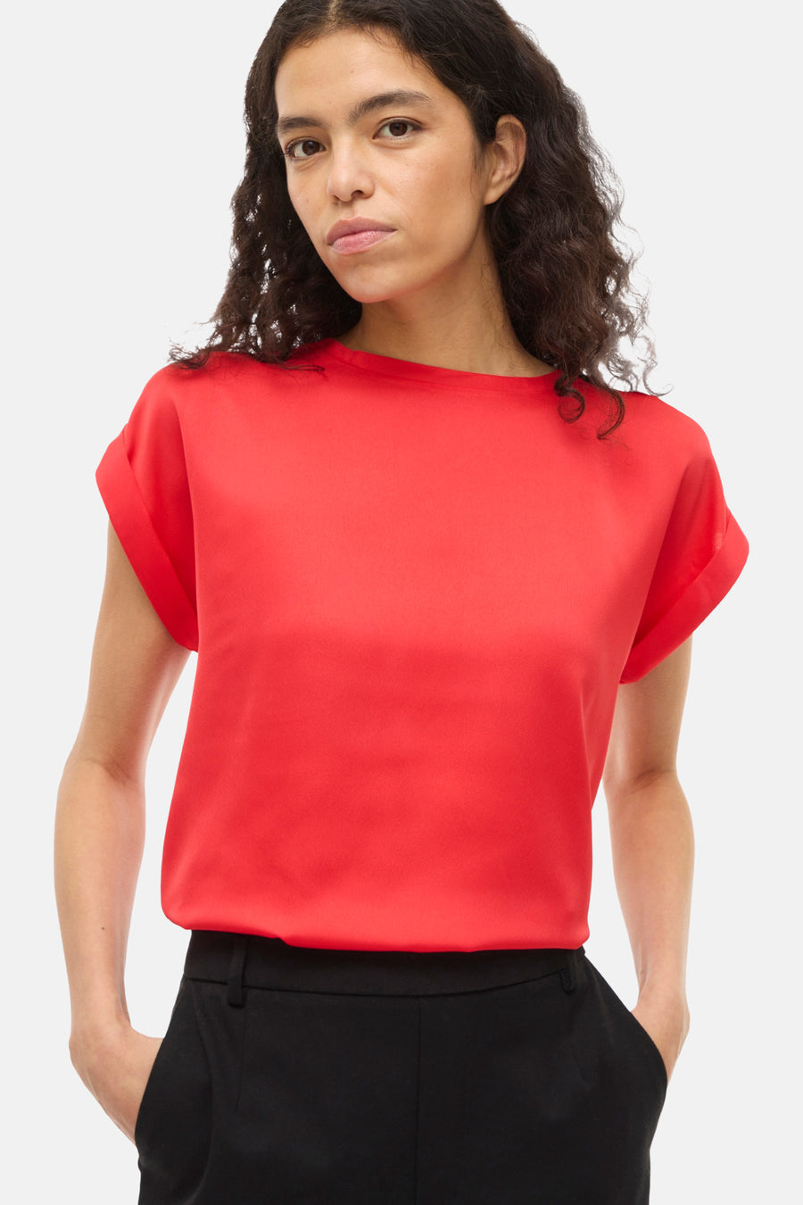 T-shirt rouge à manches courtes de VILA, porté avec un pantalon noir et les mains dans les poches.
