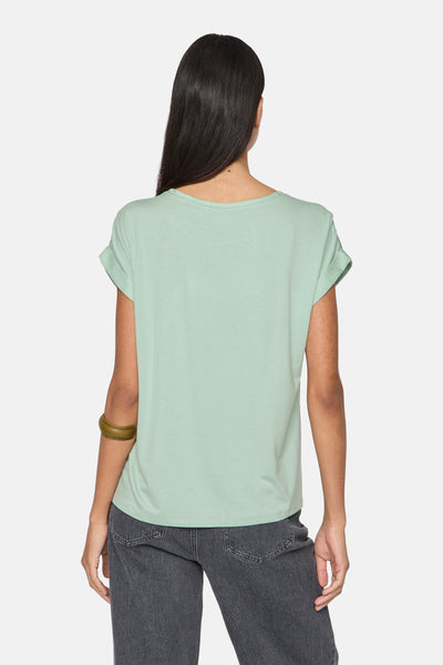 Groen T-shirt met korte mouwen van VILA, gedragen met een grijze jeans en een olijfgroen armbandje.