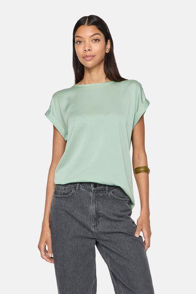 Effenchemise met korte mouwen in effen groen van VILA®, gedragen met een donkergrijze spijkerbroek en een olijfgroene armband.