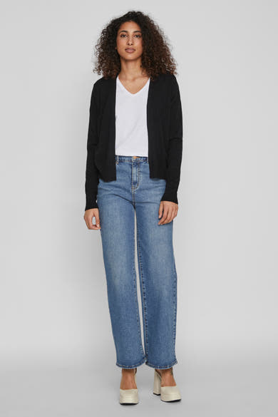 Gilet noir de VILA, porté sur un t-shirt blanc et un jean bleu large avec des talons compensés.