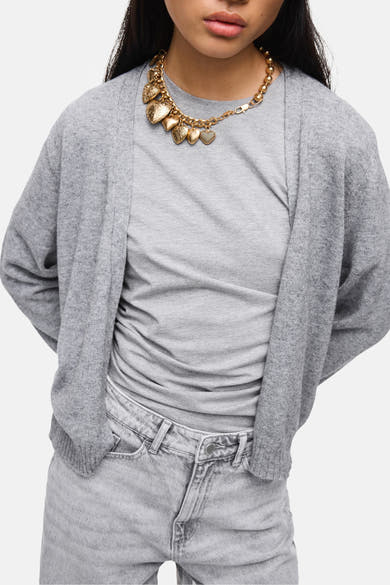 Cardigan gris de VILA, porté sur un t-shirt gris avec un collier doré à breloques en forme de cœur.