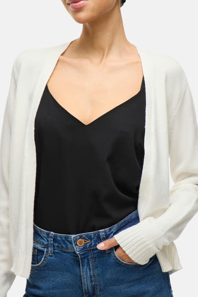 Cardigan blanc de VILA, porté sur un débardeur noir et un jean bleu.