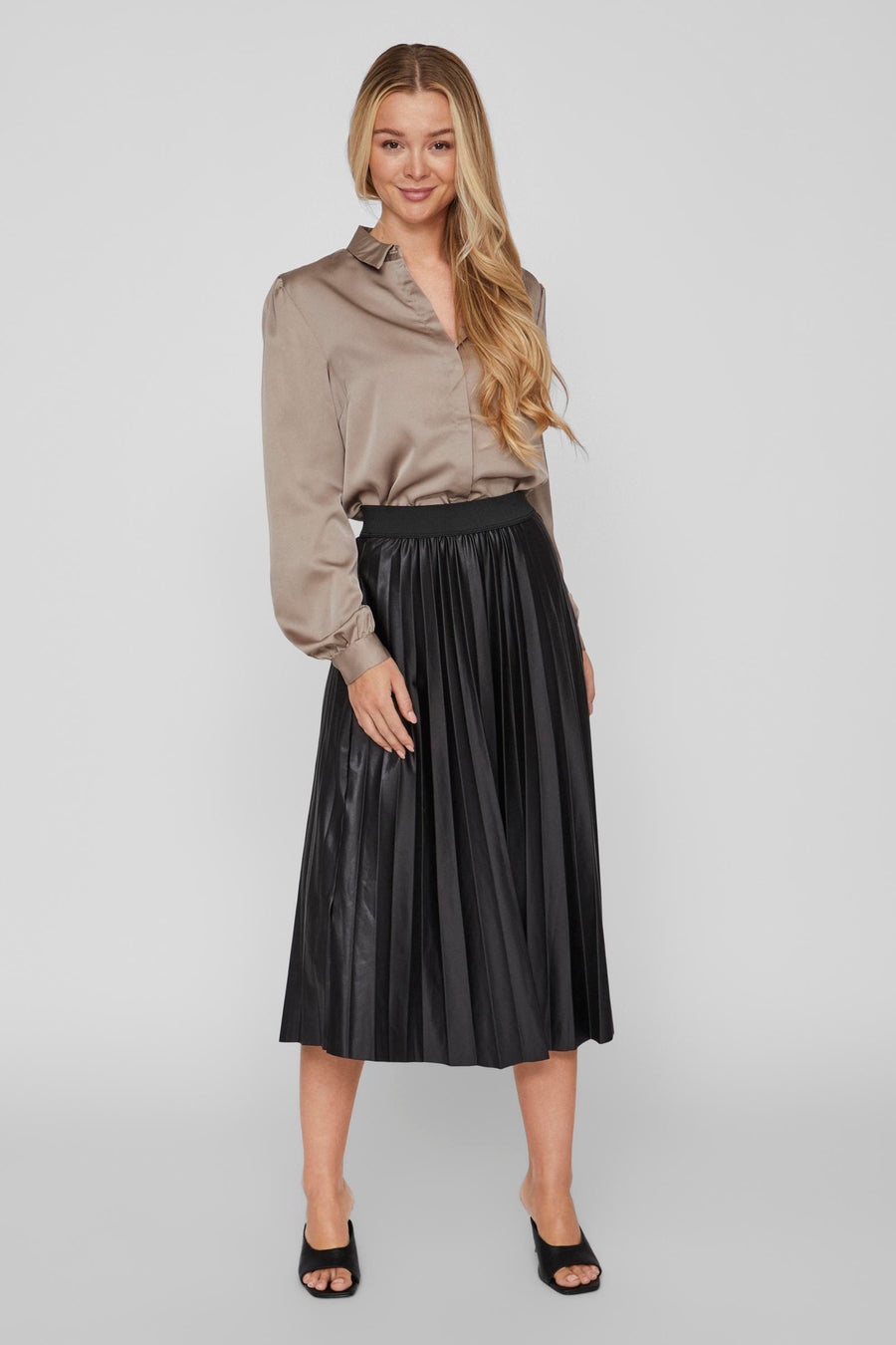 Zwarte geplooide midi-rok van VILA®, gedragen met een taupekleurige satijnen blouse en zwarte muiltjes.
